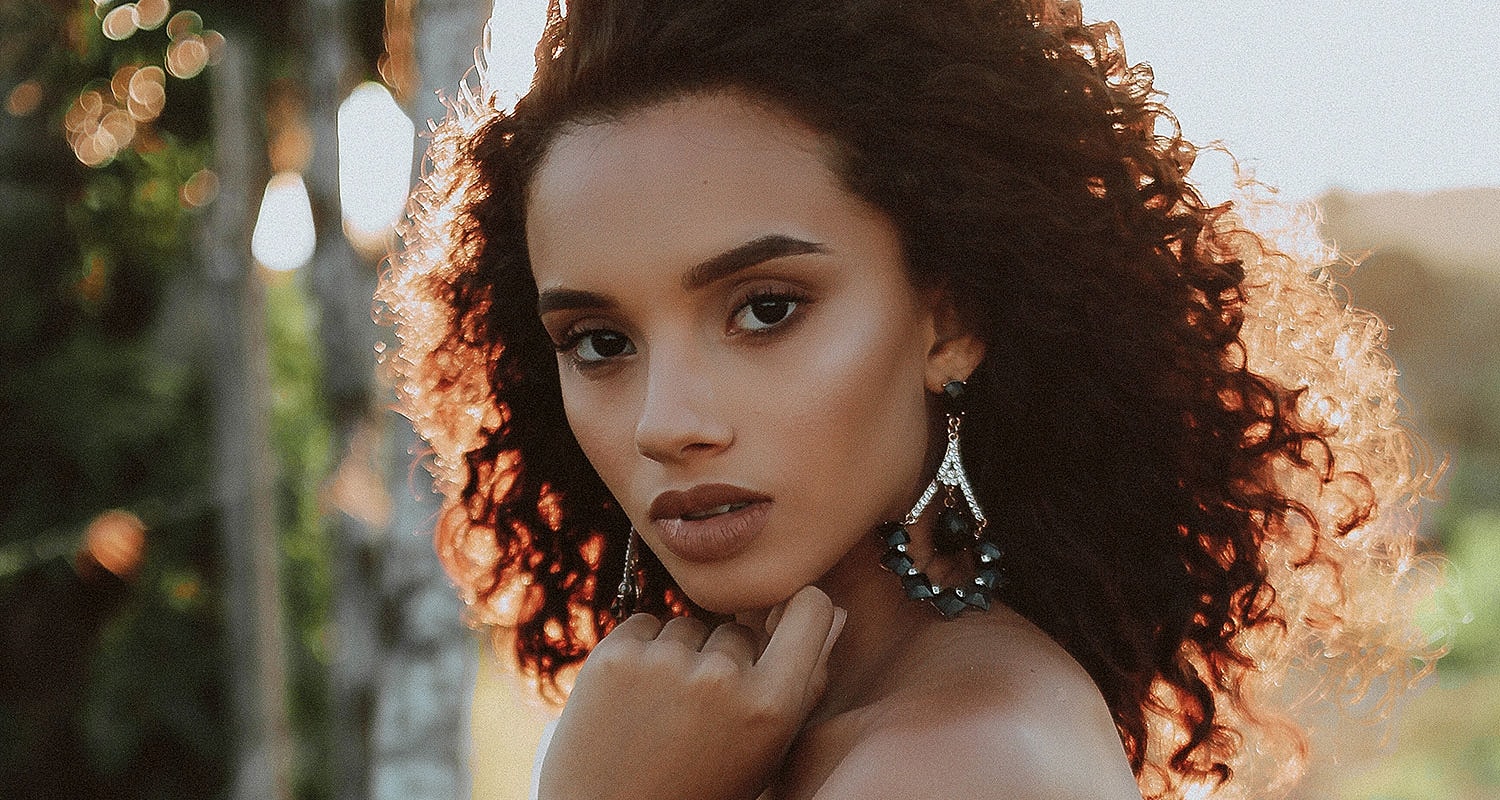 Woman with curly hair and earrings outdoors.