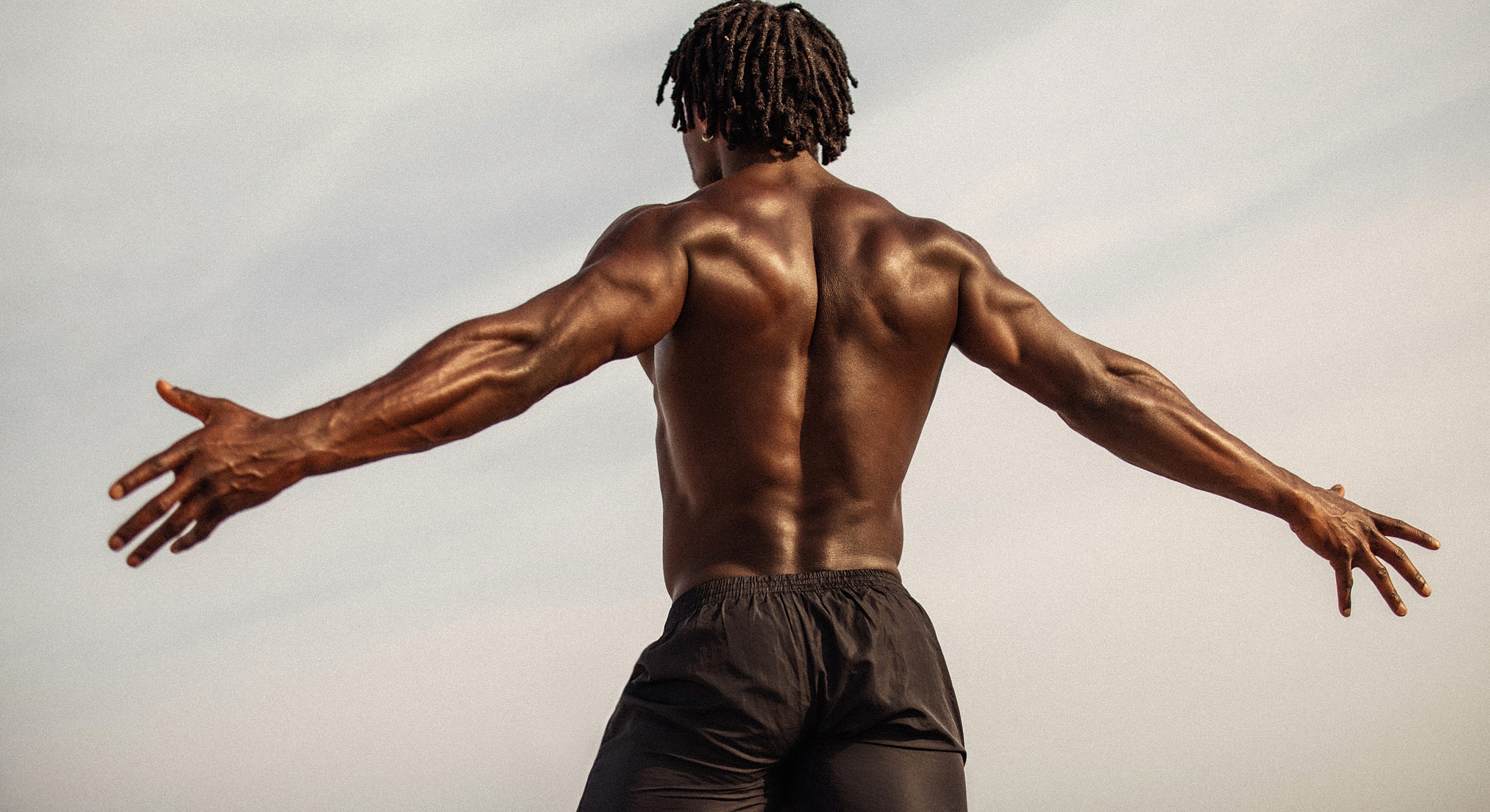 Muscular man standing with arms outstretched.
